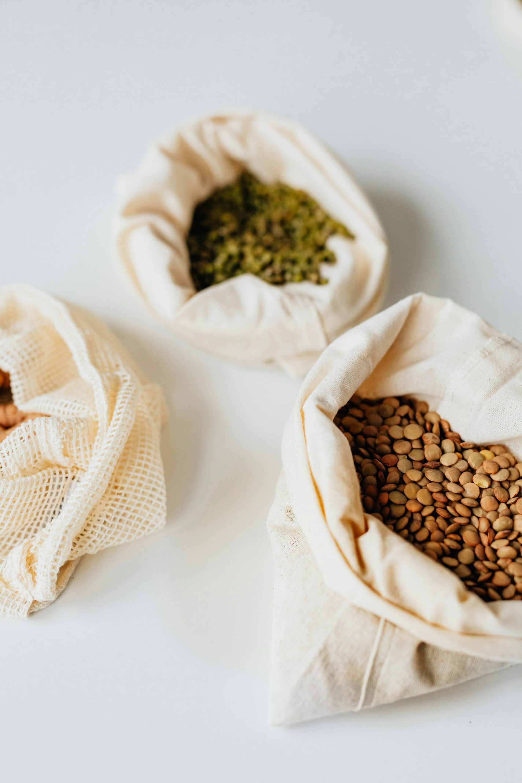 Top view of various pulses in cloth bags on white background, perfect for illustrating sustainable food storage.