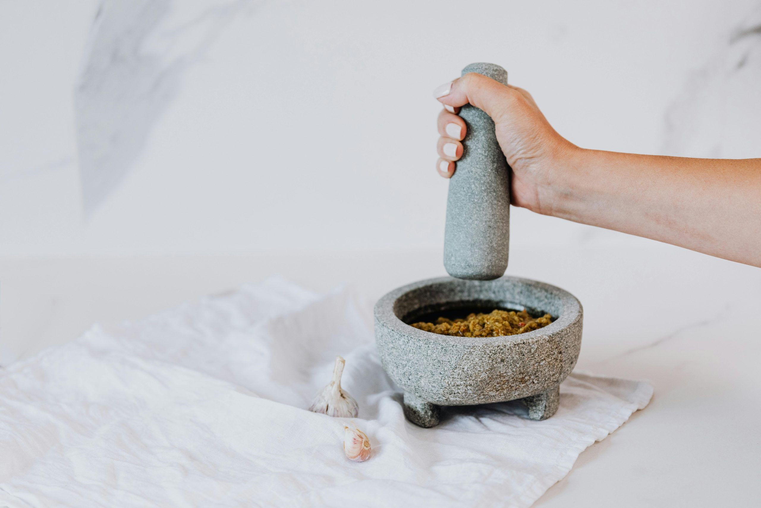 A hand using a stone mortar and pestle to make pesto with fresh ingredients.