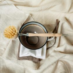 Eco-friendly wooden brush and ceramic bowl on linen fabric for a rustic kitchen vibe.